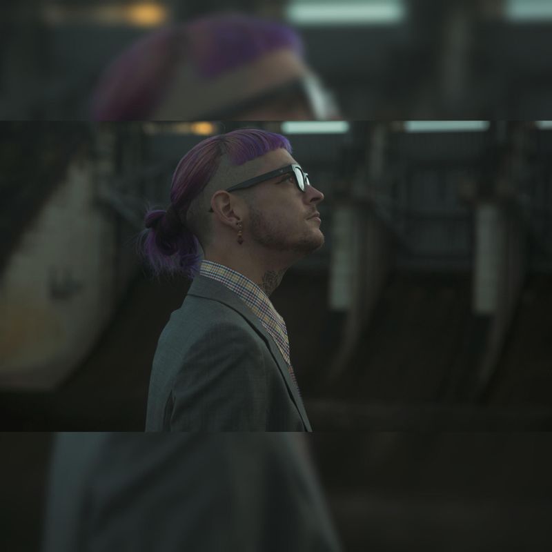 Joshy in profile wearing tinted glasses and a green suit, photographed in low warm light.